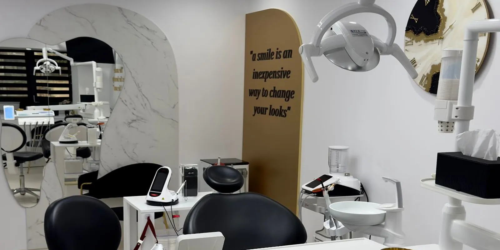Sala de tratament Andra Dent: oglinda în arcadă din marmură, panoul auriu cu citatul „a smile is an inexpensive way to change your looks”, unitul dentar negru.